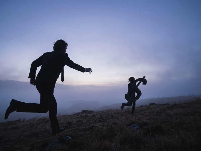 Silhouetted man in a suit chasing a figure carrying a dollar sign across a twilight hillside
