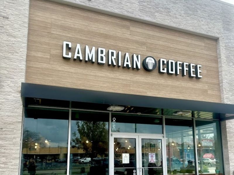 Storefront of Cambrian Coffee in a Spring Branch strip center, with a wood-panel facade, trilobite logo sign, and glass entry doors.