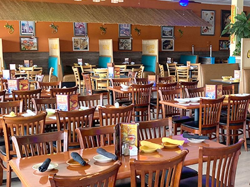 Dining room at Chavez Mexican Cafe with wooden chairs, tables set with yellow napkins, and orange walls hung with framed photos.