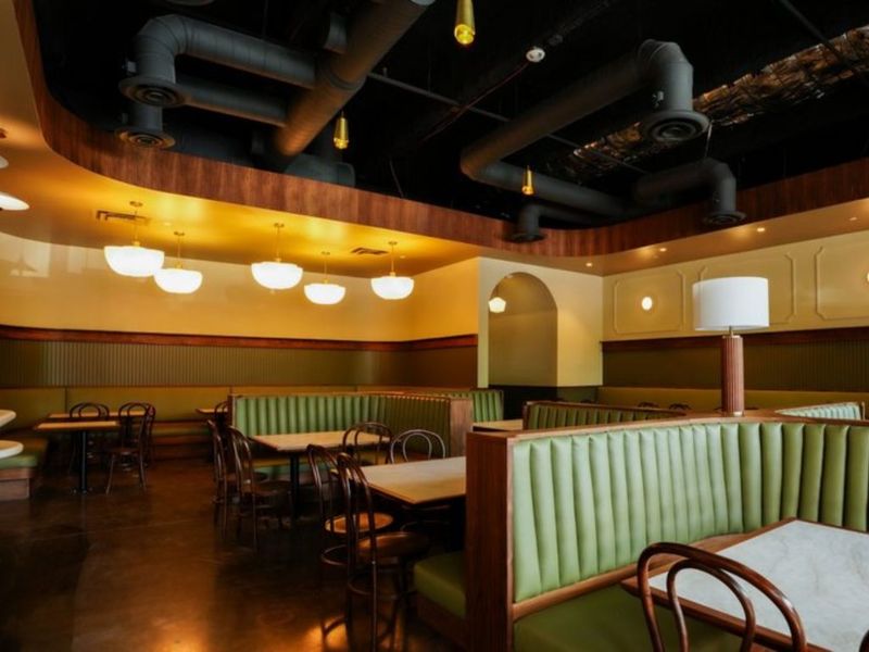 Dining room at Murray's Pizza & Wine with green tufted banquette booths, marble-topped tables, and schoolhouse pendant lights.