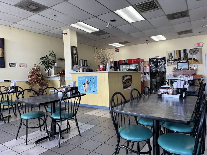 Casual dining room at Pho Luc Lac in Spring Branch, with teal-cushioned chairs, a yellow service counter, and a bubble tea sign.